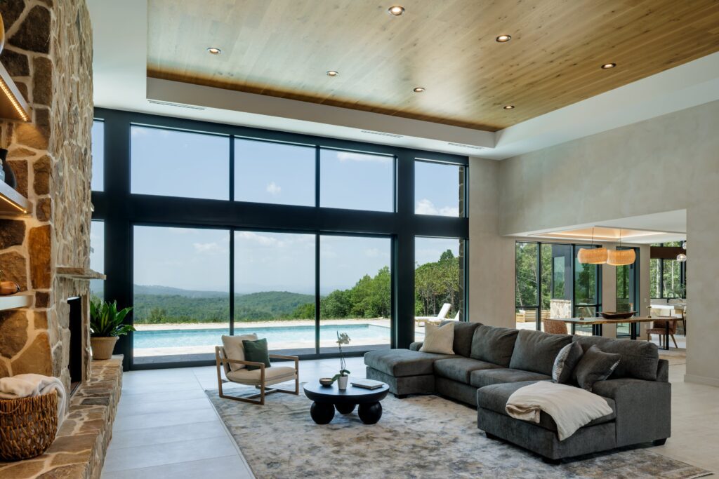 organic modern living room with natural materials including locally sourced stone on the fireplace and cedar plank wood on the ceiling. The 17' glass to floor windows give panoramic Blue Ridge Mountain views.