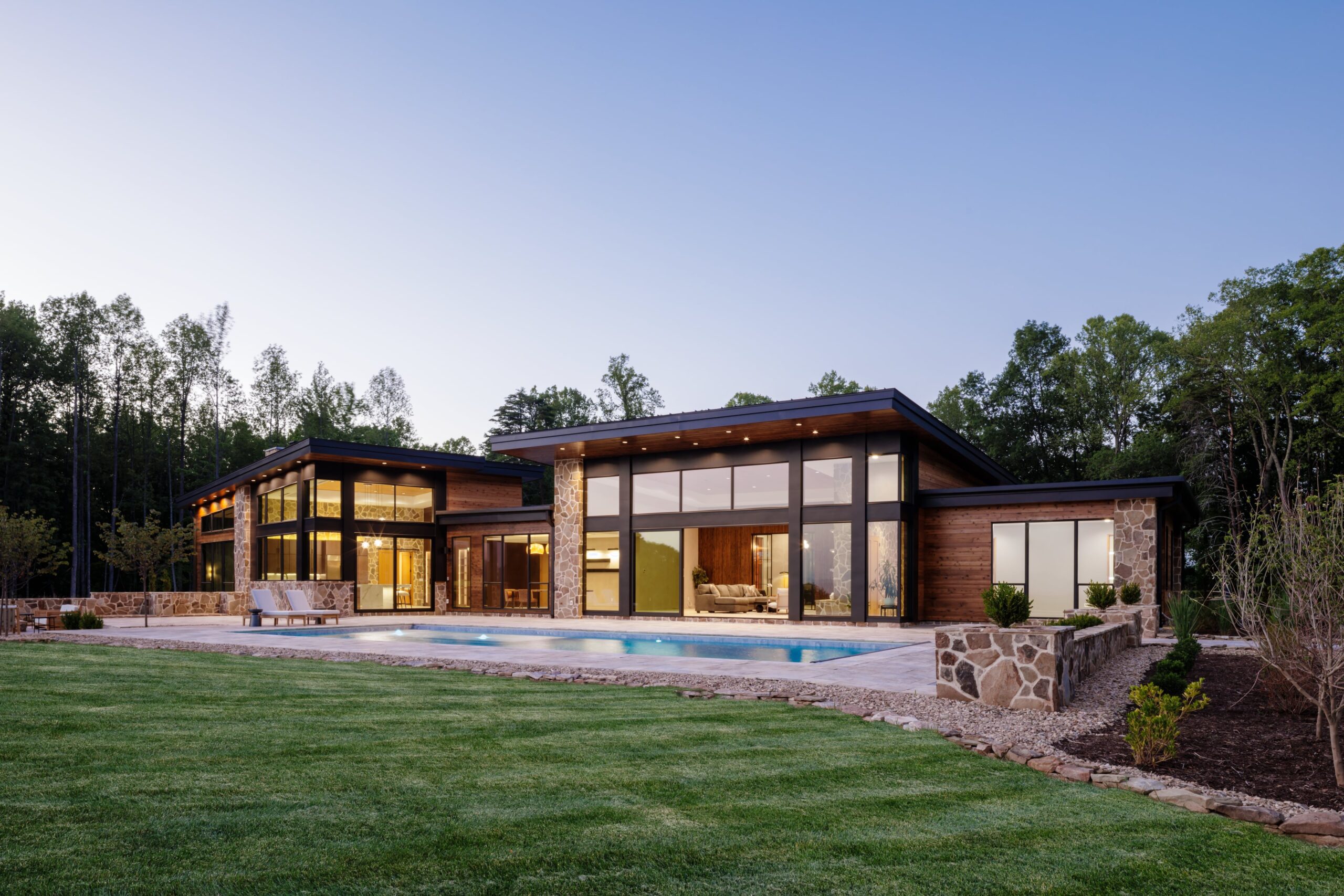 back of organic modern home in Charlottesville, VA at dusk with the 17' glass walls showing and pool sparkling at sunset.